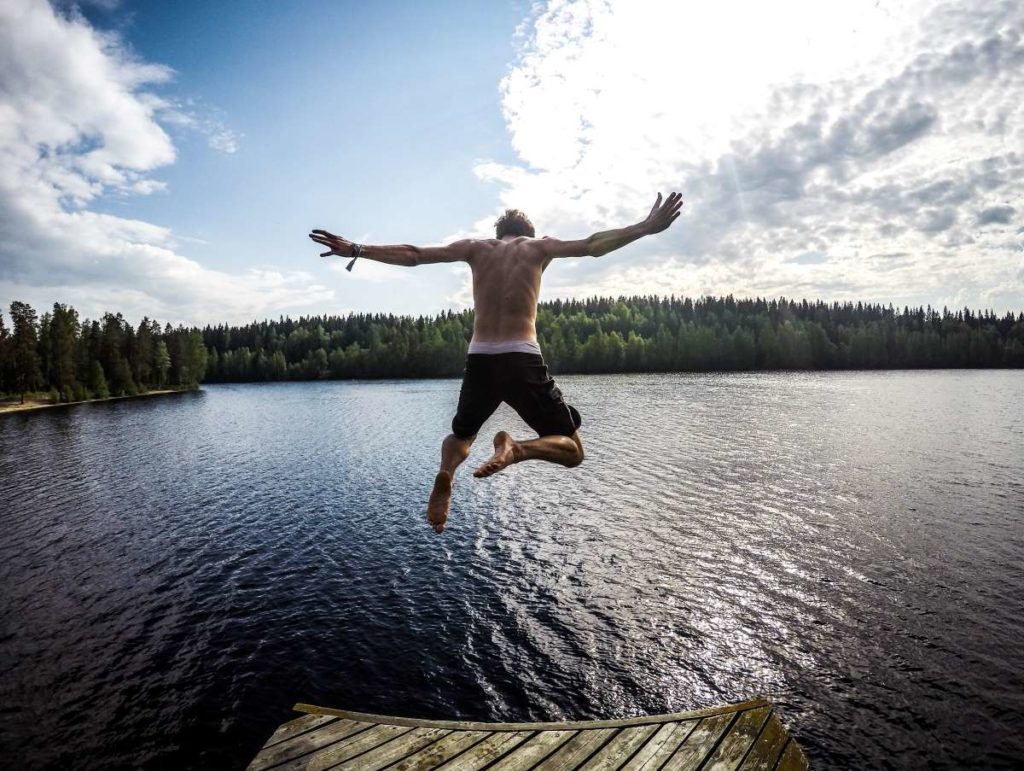 Italialainen nuori mies hyppää laiturilta järveen. 